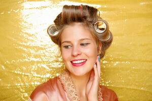 Beautiful girl in hair curlers isolated on gold photo