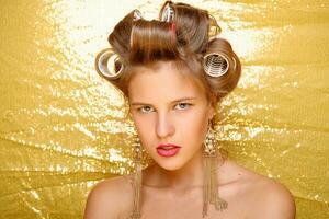 Beautiful girl in hair curlers isolated on gold photo