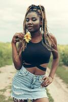 africano americano niña en un campo de amarillo flores a puesta de sol foto