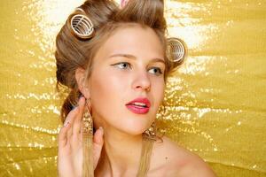 Beautiful girl in hair curlers isolated on gold photo