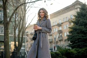 woman in trench coat walking and drinking coffee from paper cup photo