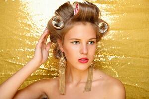 Beautiful girl in hair curlers isolated on gold photo