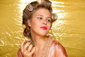 Beautiful girl in hair curlers isolated on gold photo