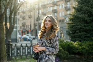 woman in trench coat walking and drinking coffee from paper cup photo