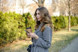 woman in trench coat walking and drinking coffee from paper cup photo