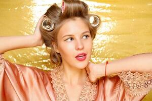 Beautiful girl in hair curlers isolated on gold photo