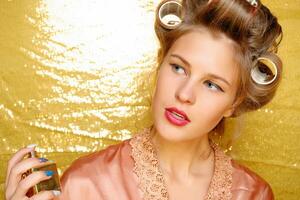 Beautiful girl in hair curlers isolated on gold photo