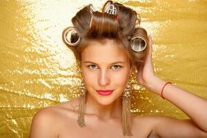 Beautiful girl in hair curlers isolated on gold photo