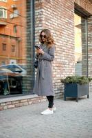 woman in trench coat walking and drinking coffee from paper cup photo