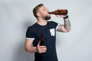 Brutal bearded male with tattooed arm drinks a beer from a bottle. photo