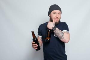 Brutal bearded male with tattooed arm drinks a beer from a bottle. photo