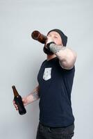 Brutal bearded male with tattooed arm drinks a beer from a bottle. photo