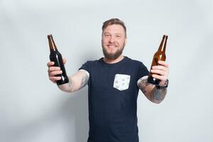 Brutal bearded male with tattooed arm drinks a beer from a bottle. photo