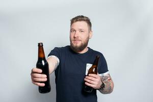 Brutal bearded male with tattooed arm drinks a beer from a bottle. photo