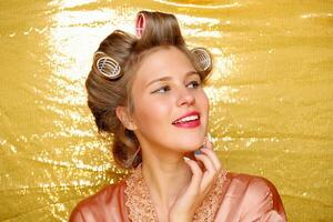 Beautiful girl in hair curlers isolated on gold photo