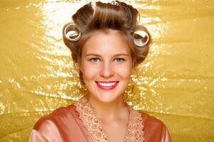 Beautiful girl in hair curlers isolated on gold photo