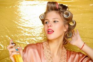 Beautiful girl in hair curlers isolated on gold photo