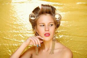 Beautiful girl in hair curlers isolated on gold photo