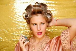 Beautiful girl in hair curlers isolated on gold photo