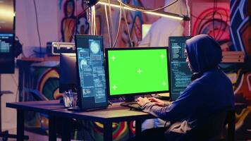 Hackers using green screen PC to code malware designed to exploit network backdoors. Cybercriminals use mockup monitor while bypassing security measures in graffiti painted bunker video