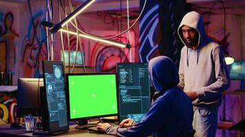 Hacker using green screen PC to do data breaches and financial theft in graffiti painted hideout. Rogue programmers using chroma key monitor for stealing users bank account credentials video