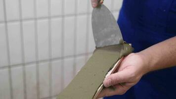 das Hände von das Fliesenleger sind Verlegung Weiß Keramik Fliese auf das Wand, bewirbt sich Klebstoff Material auf das Fliese video