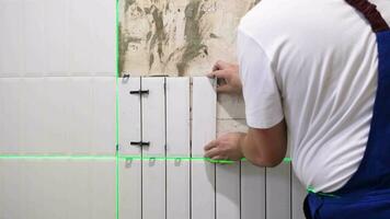 le mains de le carreleur sont pose blanc céramique tuile sur le mur, en utilisant électronique laser niveau video