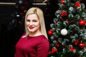 sonriente mujer cerca el Navidad árbol. de moda lujo niña celebrando nuevo año. hermosa lujo de moda rubio. foto