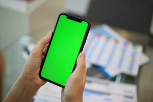 Phone green screen in hand, hand holding smartphone green screen in house, using mobile phone green screen photo