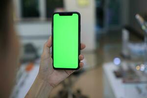 Phone green screen in hand, hand holding smartphone green screen in house, using mobile phone green screen photo