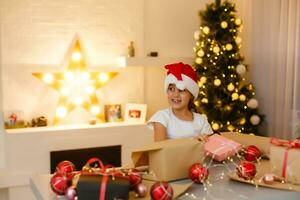 child girl in red hat preparing gifts for christmas at home, cozy holiday interior photo