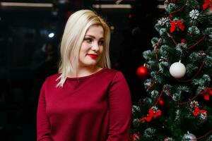 sonriente mujer cerca el Navidad árbol. de moda lujo niña celebrando nuevo año. hermosa lujo de moda rubio. foto