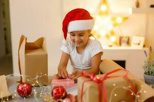 child girl in red hat preparing gifts for christmas at home, cozy holiday interior photo