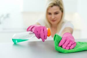 Cleanness is in trend. Pretty smiling woman wiping table with cloth and special means of washing photo