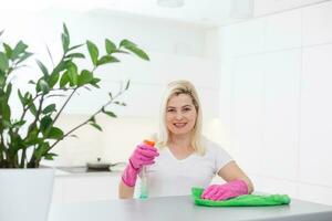 Cleanness is in trend. Pretty smiling woman wiping table with cloth and special means of washing photo