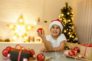 Portrait of a laughing preschool girl in Santa hat holding Christmas decoration in hands photo