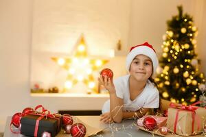 child girl in red hat preparing gifts for christmas at home, cozy holiday interior photo