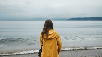 Back view of anonymous girl on raincoat standing on the sea shore. Generative AI photo