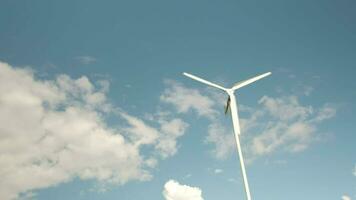 uno blanco molino en azul cielo y nubes fondo, giro en viento a generar limpiar eléctrico energía industria, natural poder recurso tecnología para sostenible ecología y ambiente conservación. video