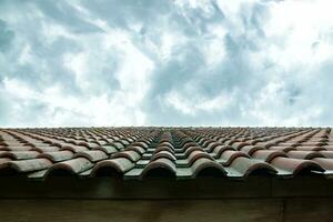 the shape of the roof of the house is made of red tiles with a bright, cloudy sky in the background photo