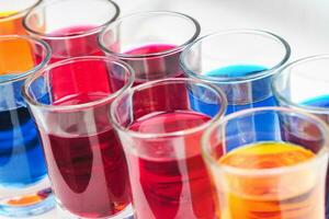 Small glasses filled with colorful water are neatly arranged on an isolated white background photo