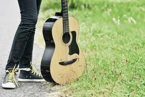 acústico guitarra y pies con Zapatos en pie en verde césped foto