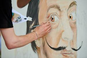 Young man artist draws with paint brush surreal man portrait on white canvas art painting festival photo