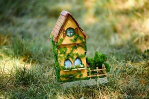 Little dollhouse on front lawn, cute small decorative house on green grass field, copy space photo