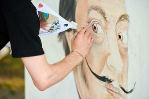 Young man artist draws with paint brush surreal man portrait on white canvas art painting festival photo