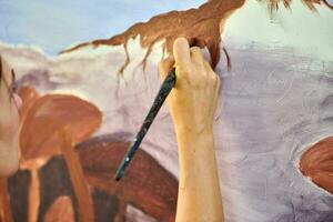 Girl artist hand holds paint brush and draws abstract surreal landscape on canvas photo