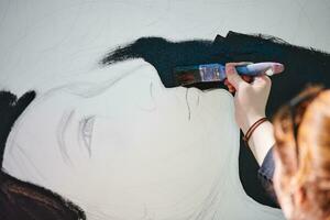 Woman artist draws with paint brush surreal girl portrait on white canvas at art painting photo
