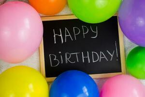 Inscription on a blackboard Happy Birthday. Multicolored balloons around the board. Preparing for the birthday. photo