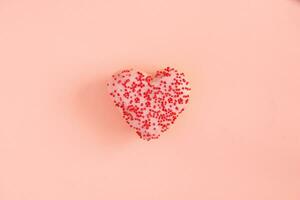 Heart-shaped donut with pink icing on a pink background. photo