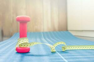 centímetro cinta alrededor un pesa en un yoga estera. peso pérdida concepto foto